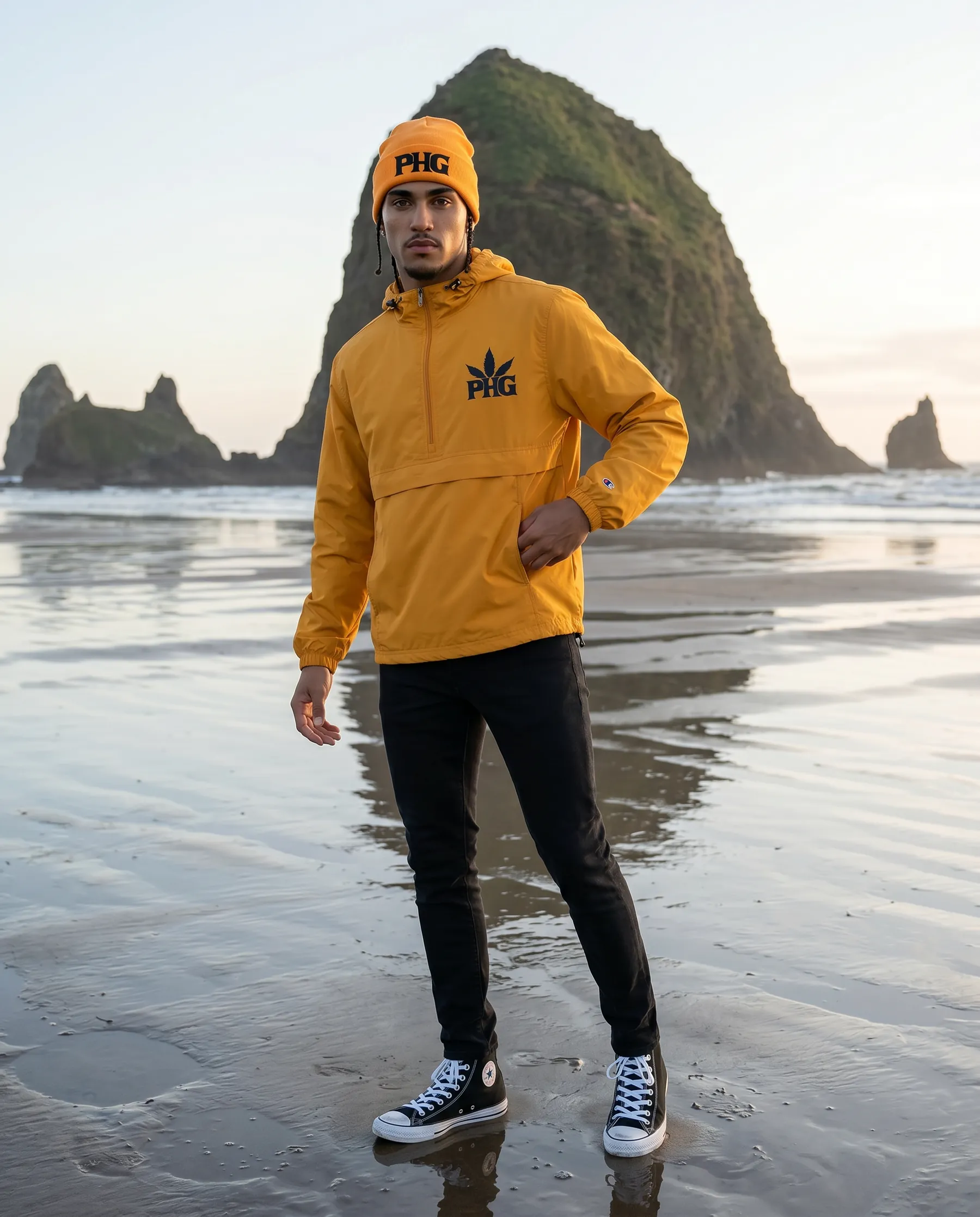 A member in a yellow PotHead Gang hoodie on a beach beneath sea stacks.