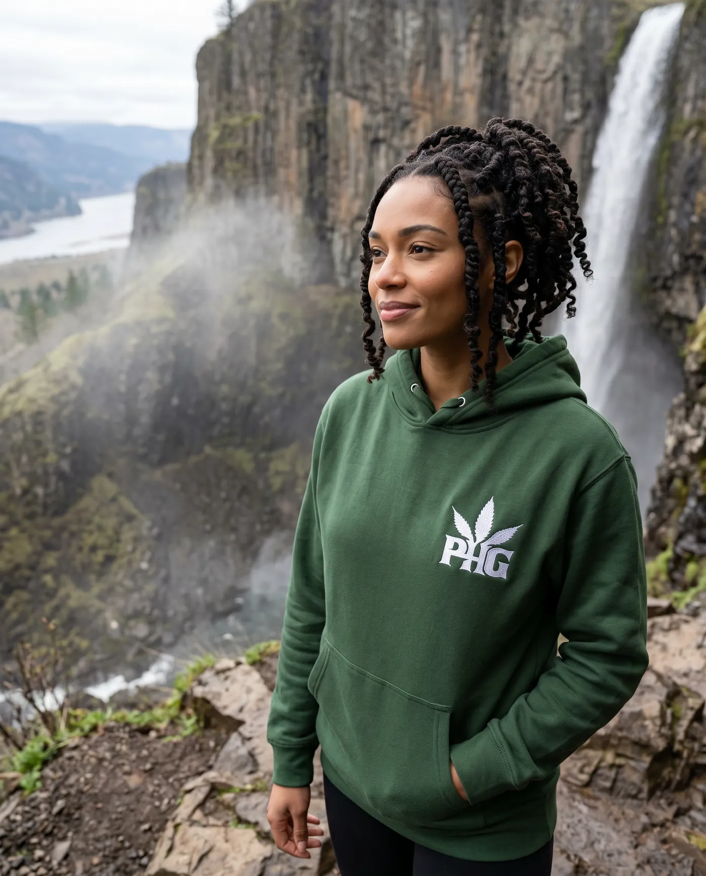 A member in a green PotHead Gang hoodie beside a waterfall.